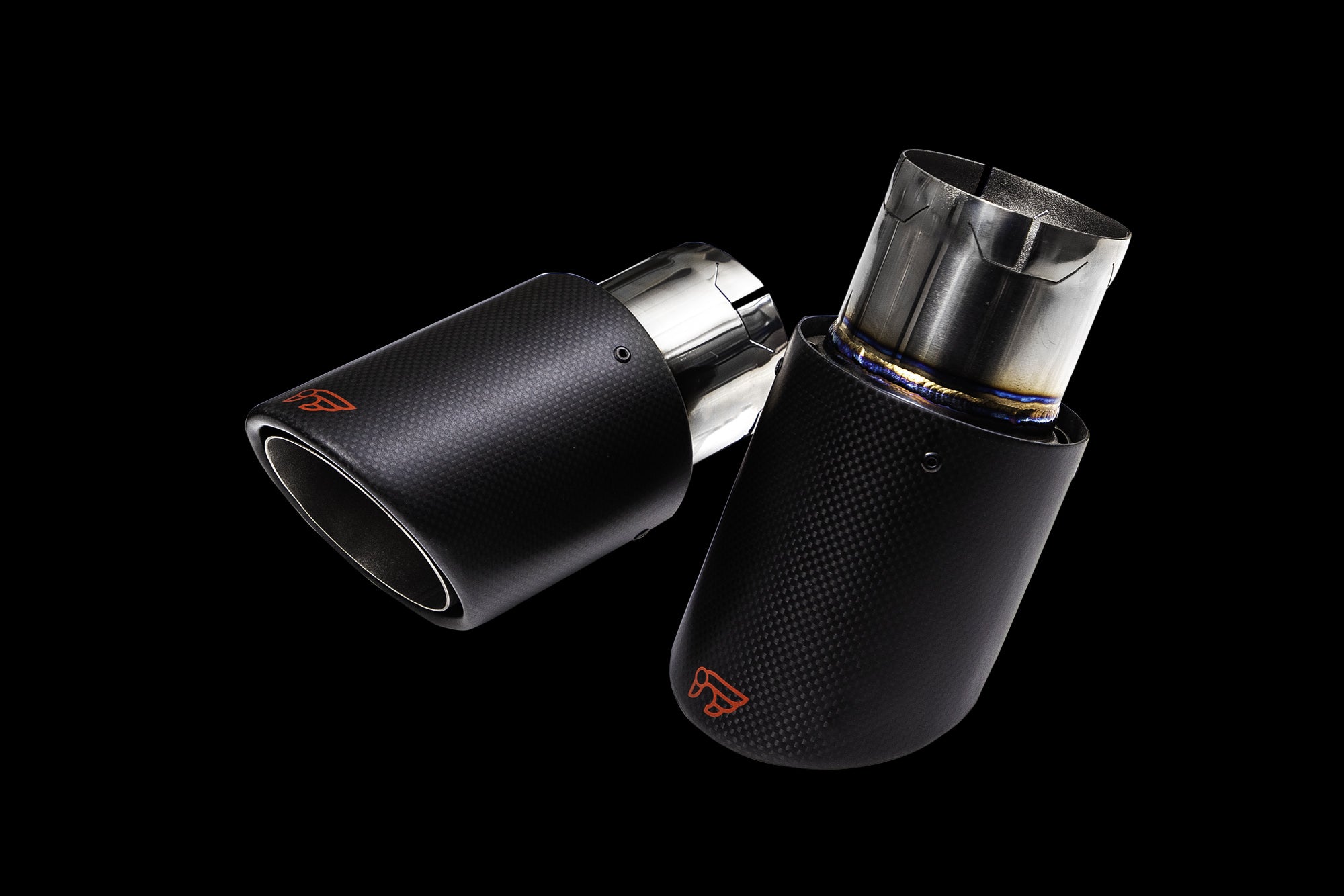 A front view of the carbon fiber tips of the IPE SS Cat-Back Exhaust System with Remote Control for Audi A4 / A5 B9 2.0 TFSI Quattro 2016-2019 on a black background