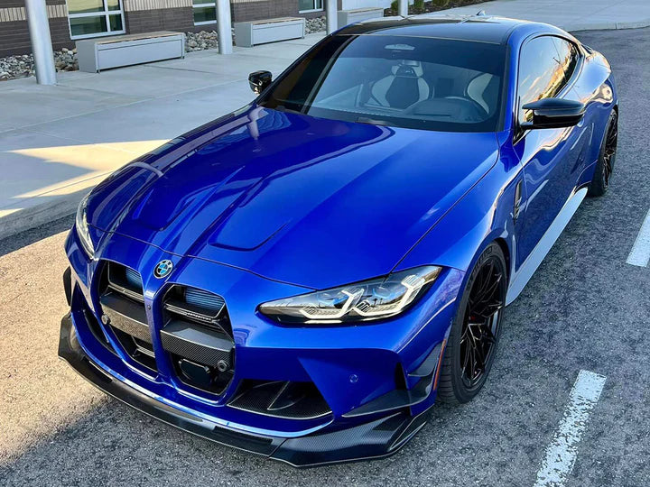 A front side view of a blue car fitted with AUTOTECKNIC DRY CARBON VERSUS FRONT AERO LIP - BMW G80 M3 | G82/ G83 M4 2021+