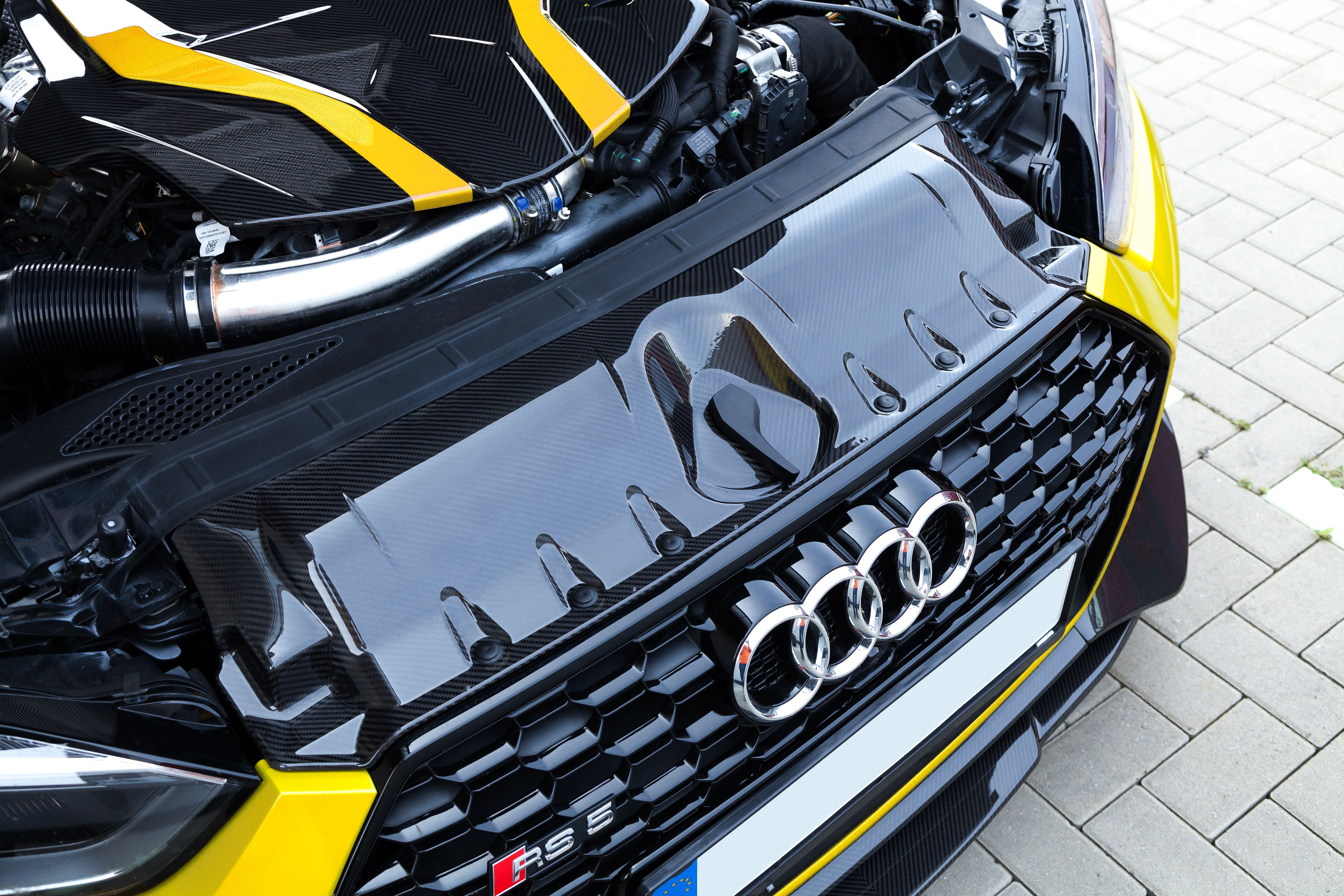 Capristo carbon fiber lock cover above the grille of a yellow Audi RS5 F5
