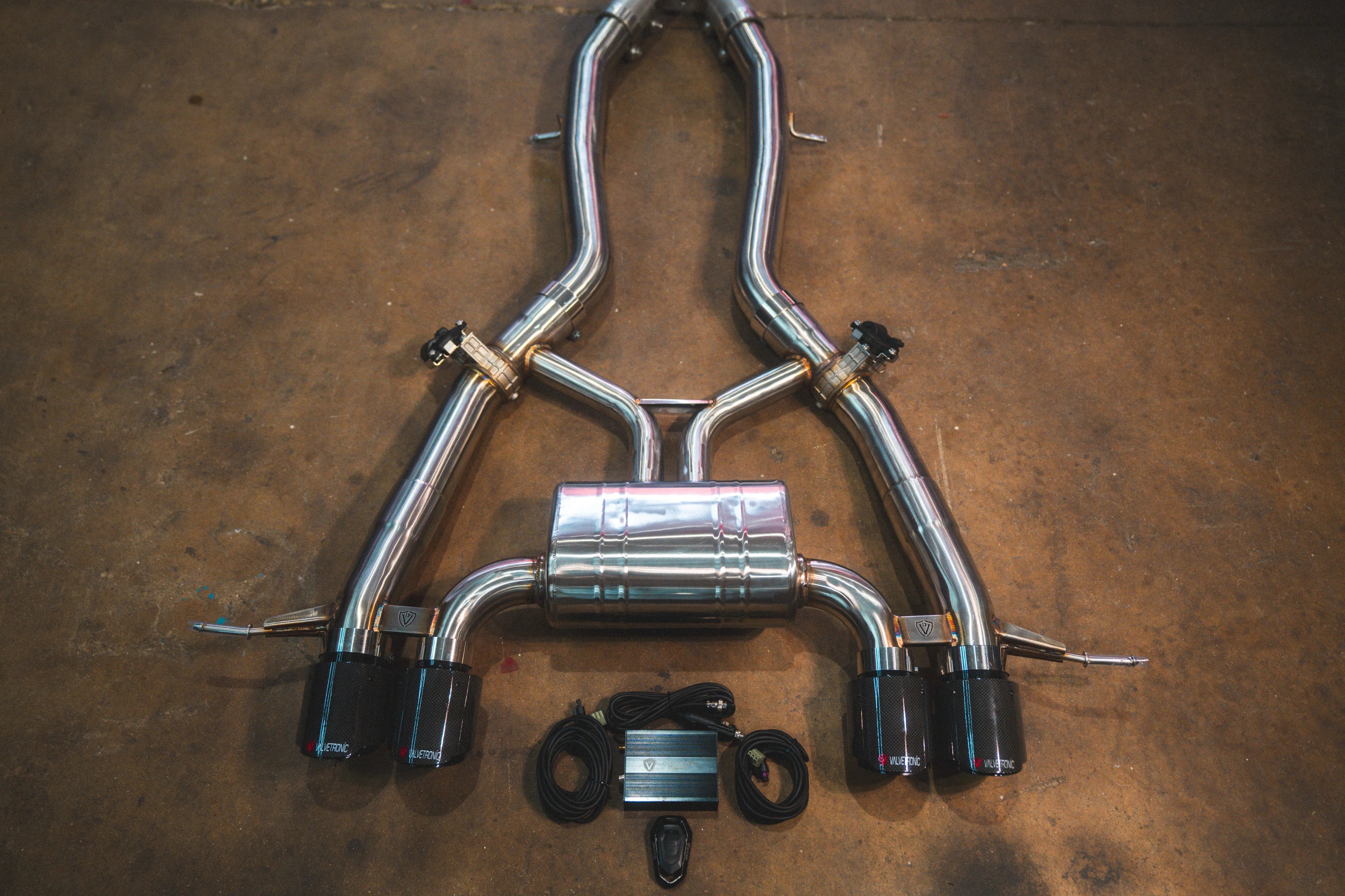 A close up view of axle-backstainless steel valved exhaust system for a BMW G87 M2 featuring a quad-tip configuration with glossy black exhaust tips and electronic control accessories.