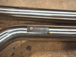 A close view of a part of Valvetronic Designs Valved Sport Exhaust System, showing the brand's logo, on the ground (for BMW F87 M2).