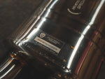 A close view of a part of Valvetronic Designs Valved Sport Exhaust System, showing the brand's logo, on the ground (for BMW F87 M2).