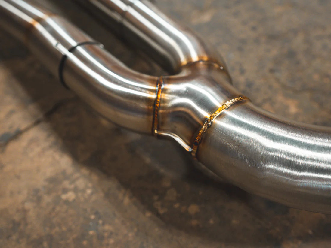 A close up view of Valvetronic Designs Valved Sport Exhaust System pipes on the ground (for BMW G20/G22 M340i/M440i).