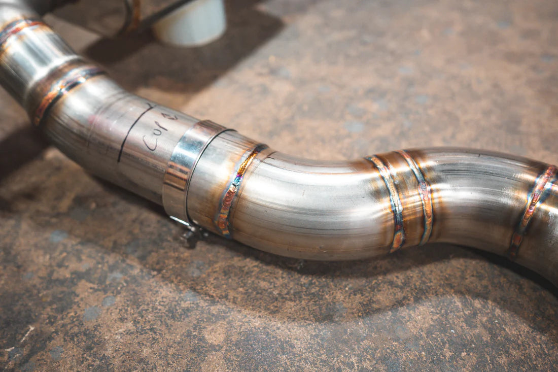 A close up view of Valvetronic Designs Valved Axleback Exhaust System's pipes on the ground (for BMW G20/G22 330i/430i). 