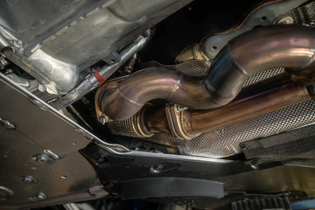 A close up view of Valvetronic Designs Valved Sport Exhaust System fitted on a lifted blue car from beneath (for BMW G87 M2).