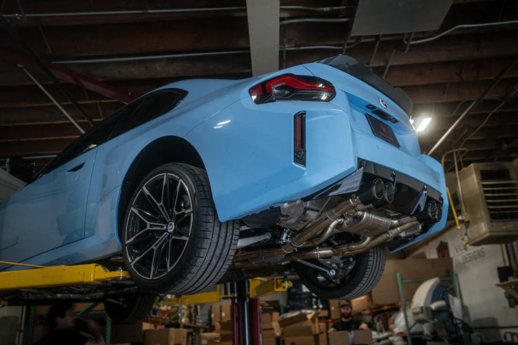 A side overview of Valvetronic Designs Valved Sport Exhaust System fitted on a lifted blue car (for BMW G87 M2).