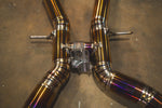 A top-down view of the midsection of the Valvetronic Designs exhaust system. This shot emphasizes the symmetrical flow of the twin titanium pipes as they merge into the center X-section, highlighting the consistent gold-anodized finish and professional weld patterns.