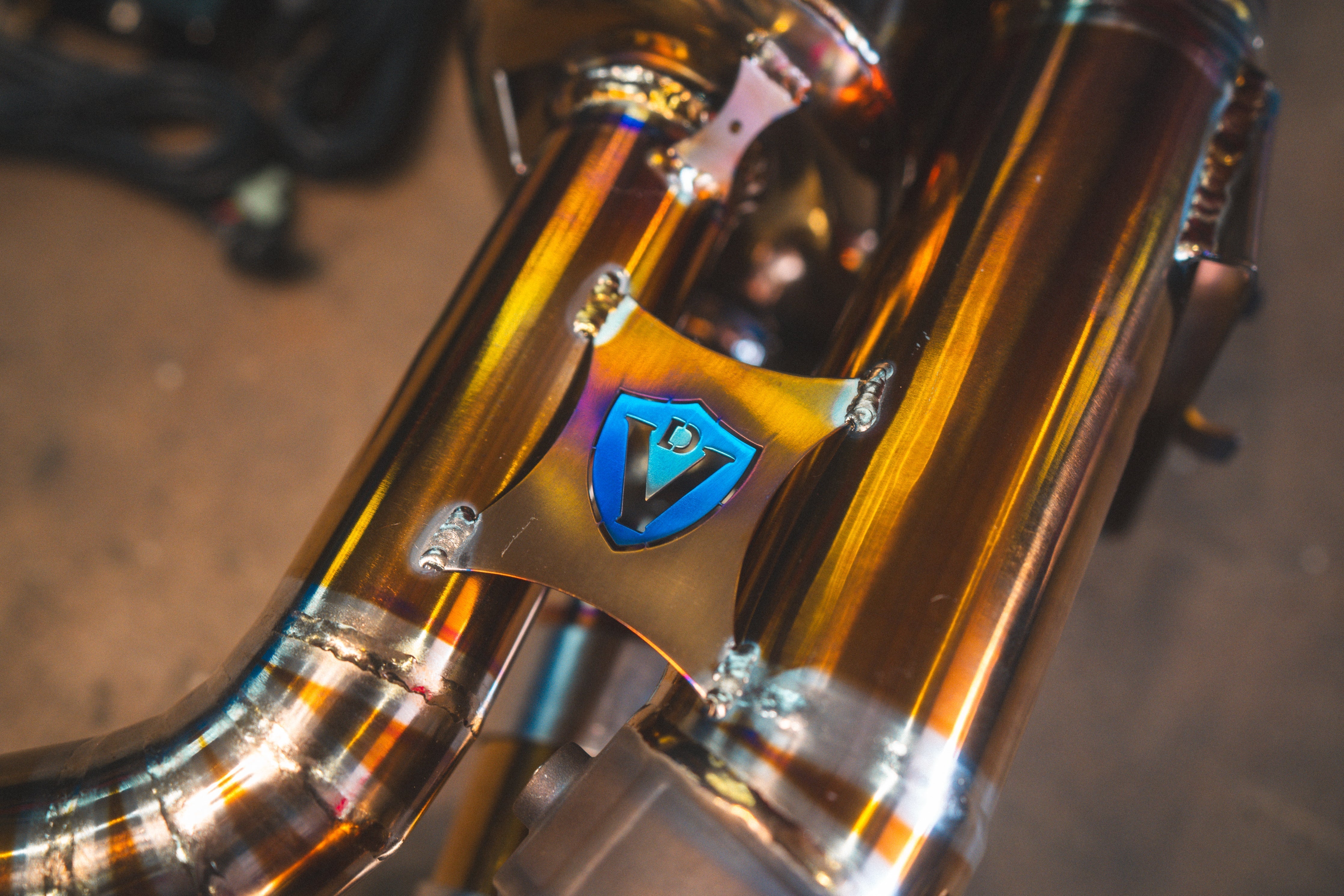 Valvetronic Designs Exhaust Porsche 992 Carrera / Turbo manufacturer gallery: blue shield brace between parallel gold-toned tubes