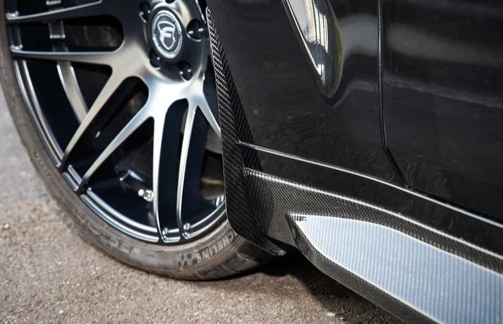 A close up view of AUTOTECKNIC CARBON FIBER FRONT SPLASH GUARDS - BMW G80 M3 | G82 M4 2021+ fitted on a black car