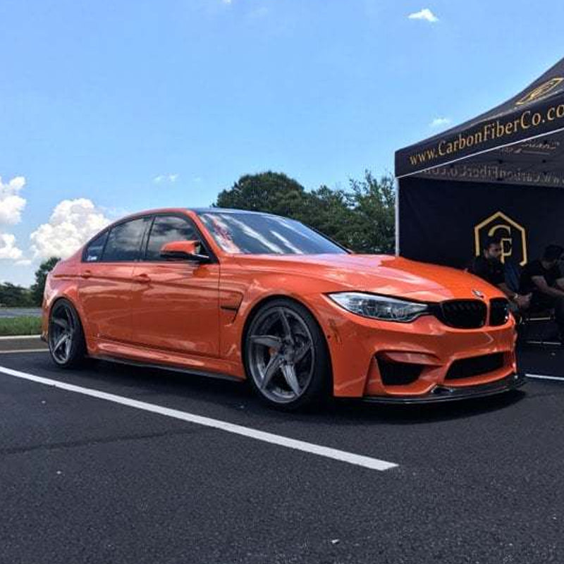 Orange BMW F80 M3 sedan at a car show, running VRSF front facing air intakes