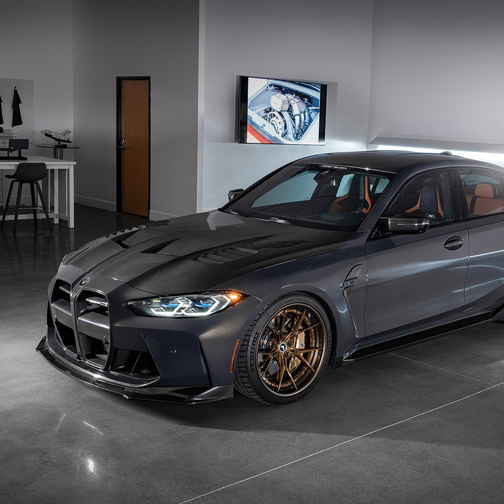 Grey G8X M3 with carbon GTS-V bonnet in garage, front 3/4 view