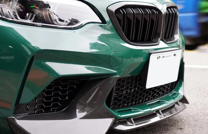 A side close up front view of AUTOTECKNIC DRY CARBON PERFORMANTE AERO SPLITTERS - BMW F87 M2 COMPETITION 2018+ fitted on a olive green car