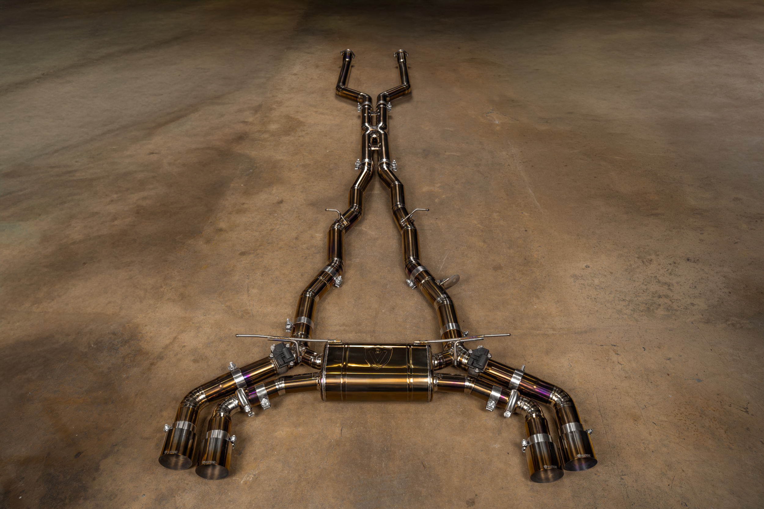 Valvetronic Designs Valved Exhaust BMW G90 M5 manufacturer gallery: complete silver-and-gold-toned exhaust laid lengthwise on the floor