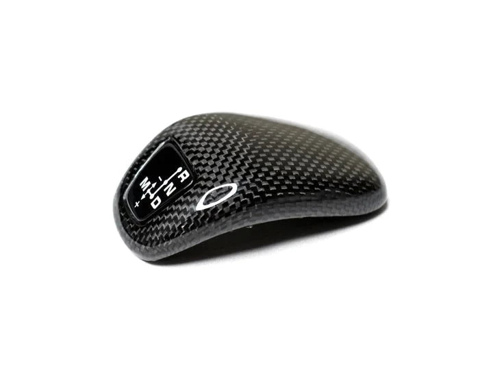 A front view of AUTOTECKNIC CARBON FIBER GEAR SELECTOR COVER - PORSCHE 971 / 971.2 PANAMERA 2017+ with white background
