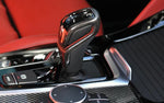 A close up view of AUTOTECKNIC CARBON FIBER GEAR SELECTOR SIDE COVERS - BMW F90 M5 2018+ fitted on a car with red interior