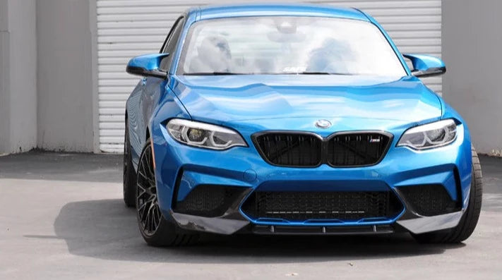 A front side wide view of AUTOTECKNIC DRY CARBON FIBER CENTER FRONT LIP - BMW F87 M2 COMPETITION 2018+ fitted on a blue car