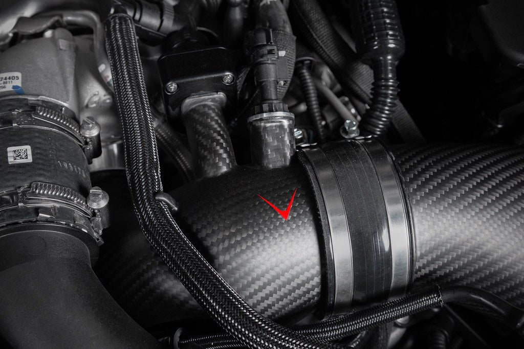 Carbon fiber turbo inlet with aluminum coupling band installed in engine bay with red arrow pointing to component - Eventuri turbo inlet for BMW G90 G99 M5