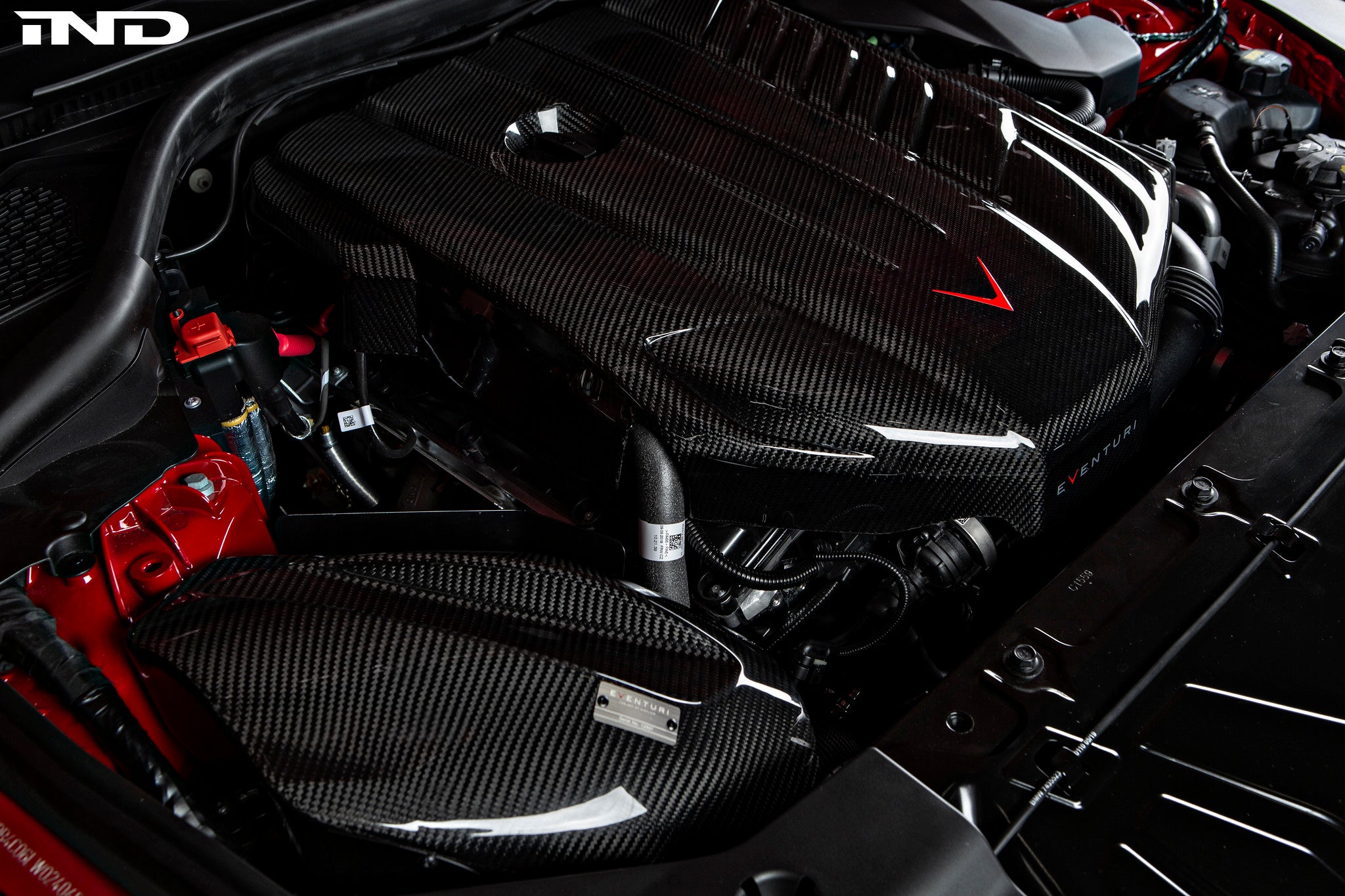 Carbon fiber engine cover with twill weave pattern installed in Toyota Supra engine bay with red arrow pointing to component - Eventuri engine cover for Toyota Supra