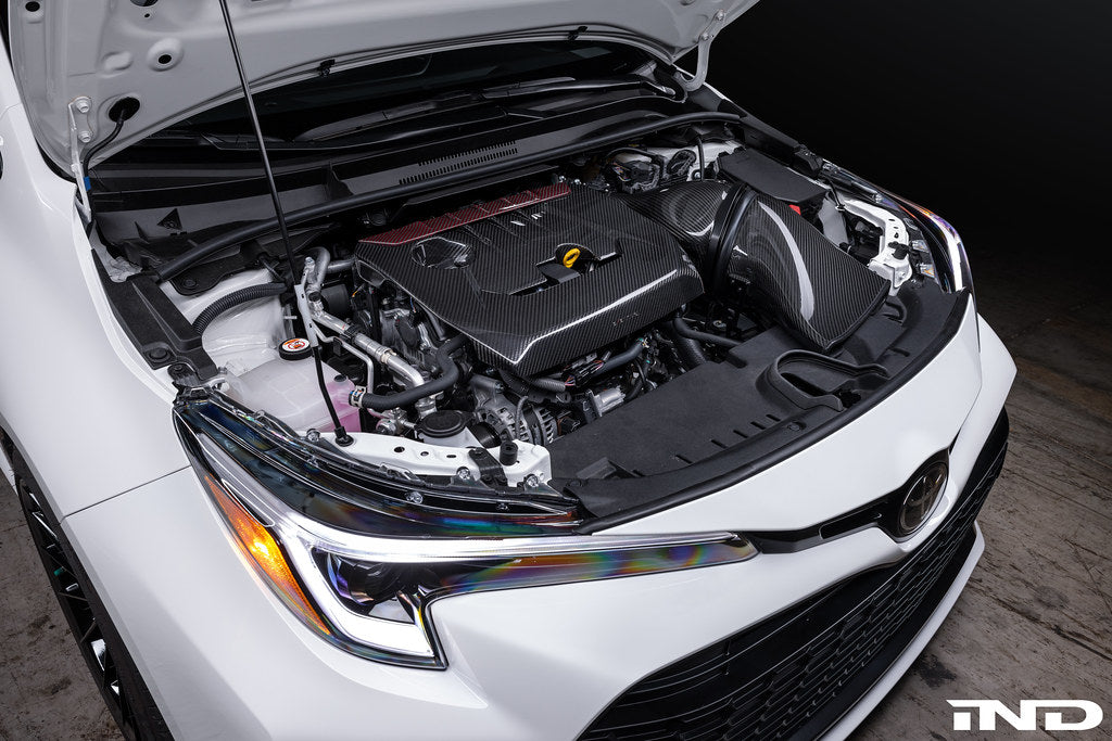 Carbon fiber intake system installed in white Toyota GR Corolla engine bay with hood open - Eventuri carbon intake for Toyota GR Corolla