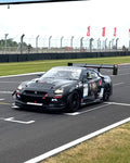 Large black carbon fiber rear wing with upright supports mounted on black race car at racetrack - APR Performance rear wing for Universal 