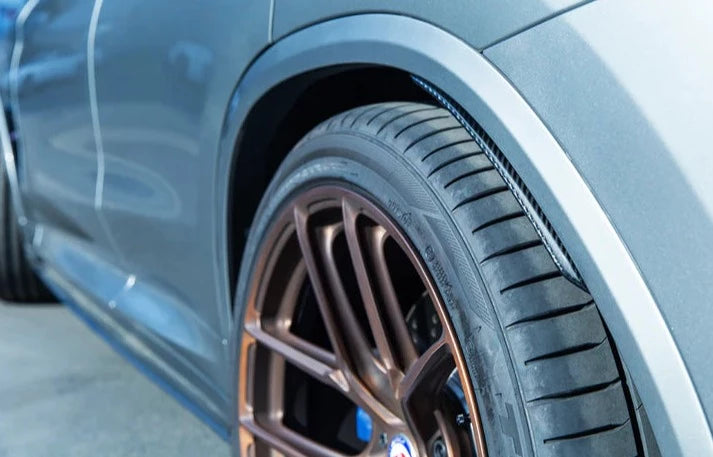 A side close up view of AUTOTECKNIC CARBON FIBER REAR SPLASH GUARDS - BMW F97 X3M | G01 X3 2018+ fitted on a blue car