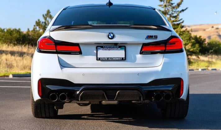 A back view of AUTOTECKNIC DRY CARBON COMPETITION SPORT REAR DIFFUSER - BMW F90 M5 2017+ fitted on a white car outside on the road