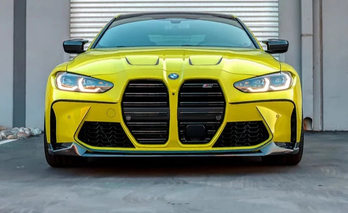A front view of a yellow car on the road fitted with AUTOTECKNIC DRY CARBON FIBER PERFORMANTE FRONT AERO LIP - BMW G80 M3 | G82/ G83 M4 2021+