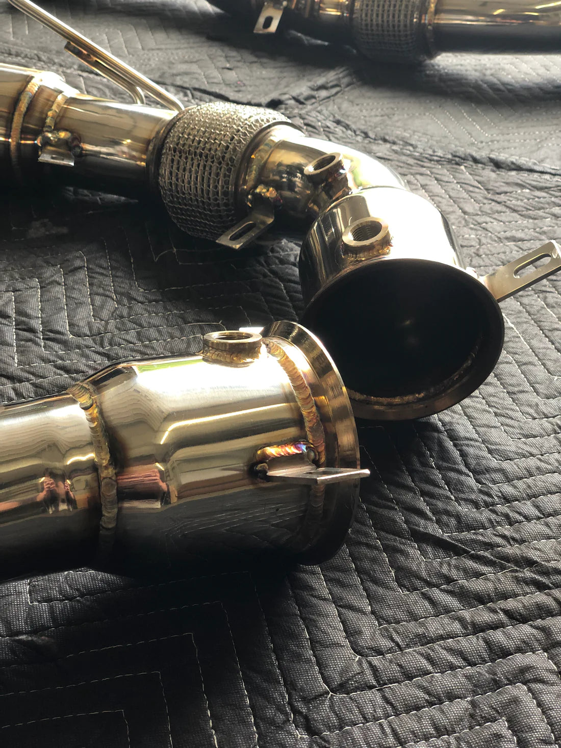 A close up view of Valvetronic Designs Free Flow Race Front Pipes on a grey carpet (for Mclaren 540C/570/600LT).