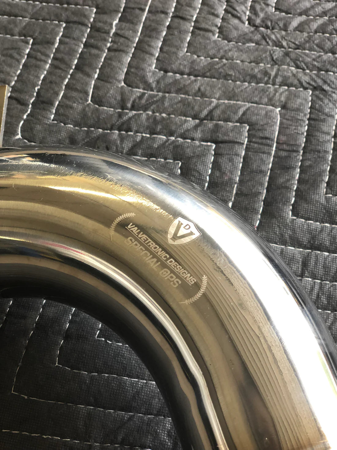 A close view of Valvetronic Designs Free Flow Race Front Pipe, showing the brand's logo, on a grey carpet (for Mclaren 540C/570/600LT).