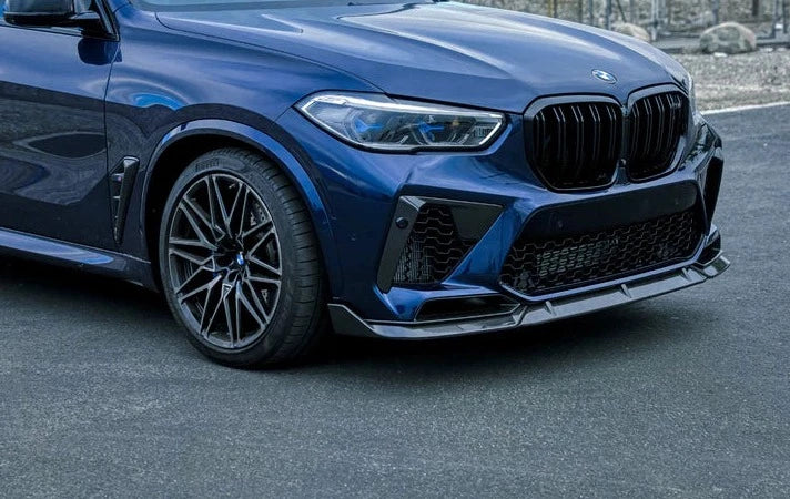 A front side view of a blue car fitted with AUTOTECKNIC PERFORMANCE DRY CARBON FRONT LIP SET - BMW F95 X5M 2019+ on the road