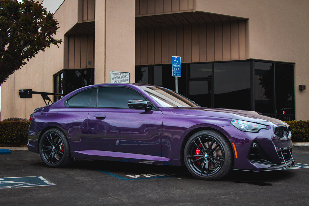 Large black carbon fiber rear wing spoiler mounted on purple BMW coupe parked in lot - APR Performance wing for BMW G42 M240i G87 M2