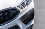 A close up view of a white car fitted with AUTOTECKNIC PERFORMANCE DRY CARBON BUMPER TRIM SET - BMW F9X M8 2019+