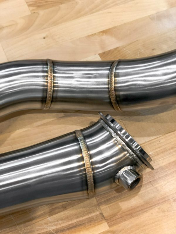 A close up view of RK Autowerks F97 F98 X3M X4M CATLESS DOWNPIPES on a wooden floor