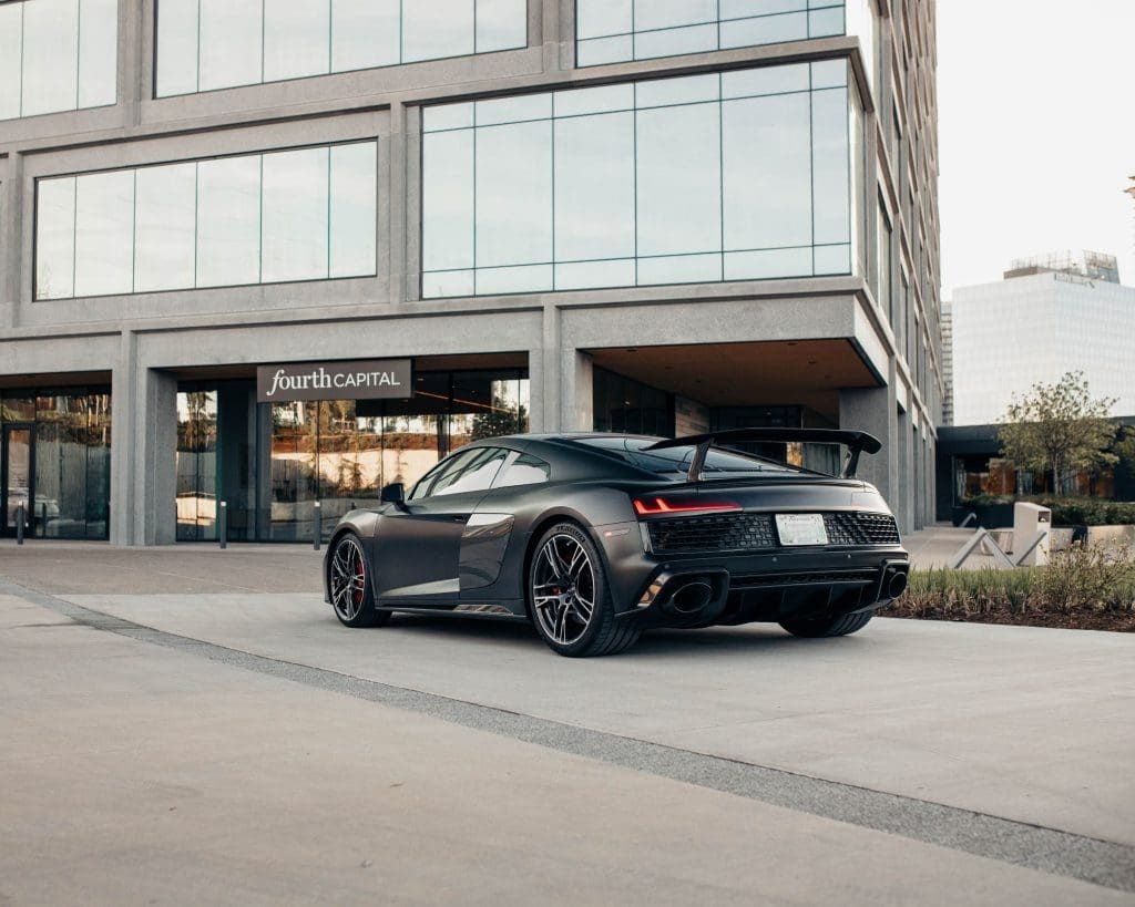 Grey Audi R8 rear three-quarter with carbon rear wing outside an office building