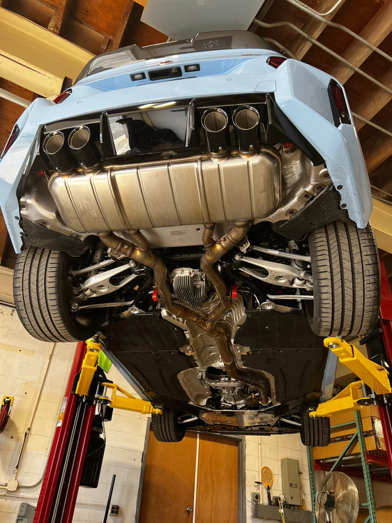 A overview of Valvetronic Designs Valved Sport Exhaust System fitted on a lifted blue car from beneath (for BMW G87 M2).