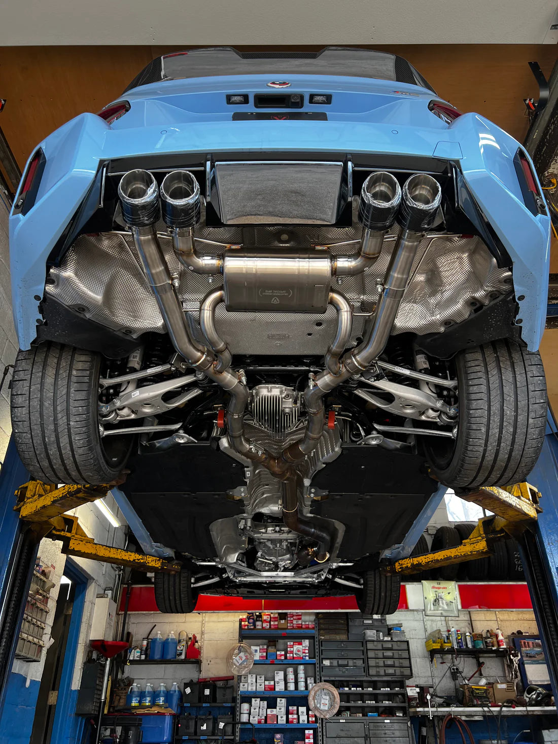 A view of Valvetronic Designs Valved Sport Exhaust System fitted on a lifted blue car from beneath (for BMW G87 M2).
