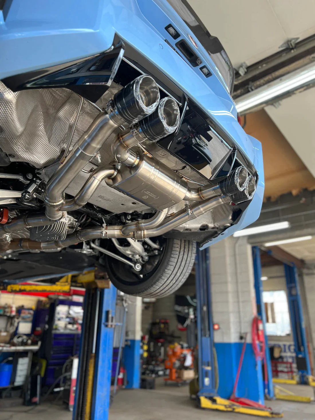 A close up of a part of Valvetronic Designs Valved Sport Exhaust System fitted on a lifted blue car from behind (for BMW G87 M2). 