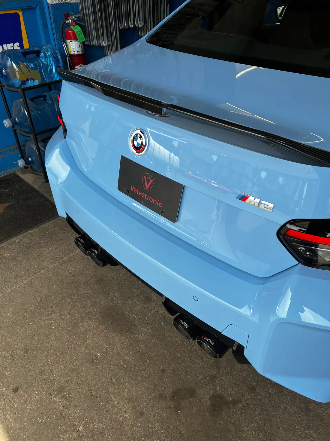 A back view of Valvetronic Designs Valved Sport Exhaust System fitted on a lifted blue car (for BMW G87 M2).