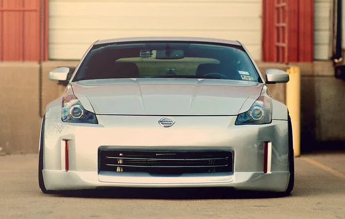 A front view of AUTOTECKNIC ABS PAINTED HEADLIGHT COVERS - NISSAN 350Z 2002-2009 fitted on a grey Nissan