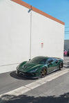 Green Ferrari F8 Tributo front three-quarter with the complete aero kit beside a wall