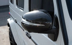 A close up view of AUTOTECKNIC REPLACEMENT DRY CARBON MIRROR COVERS - MERCEDES-BENZ X167 GLS 2019+ fitted on a white car outside on the road