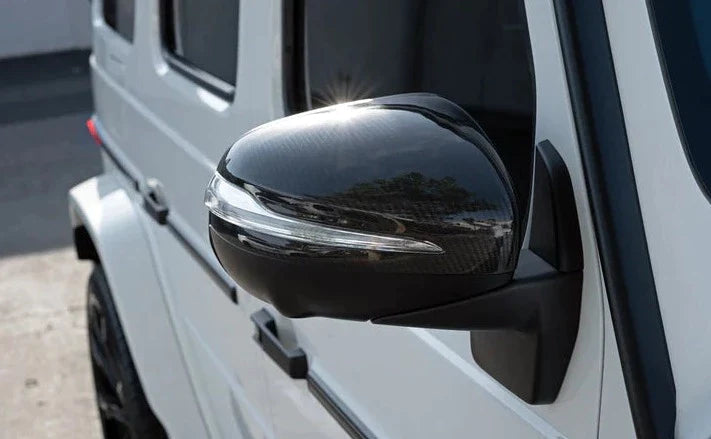A close up view of AUTOTECKNIC REPLACEMENT DRY CARBON MIRROR COVERS - MERCEDES-BENZ W167 GLE 2018+ fitted on a white car outside on the road