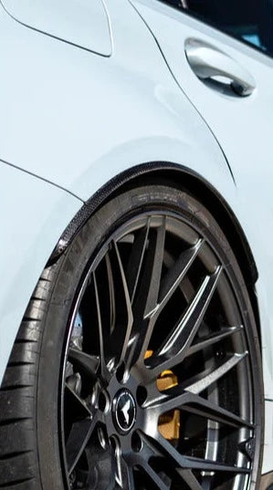 A close up view of AUTOTECKNIC CARBON FIBER REAR WHEEL ARCH EXTENSION SET - BMW G80 M3 2021+ fitted on a white car