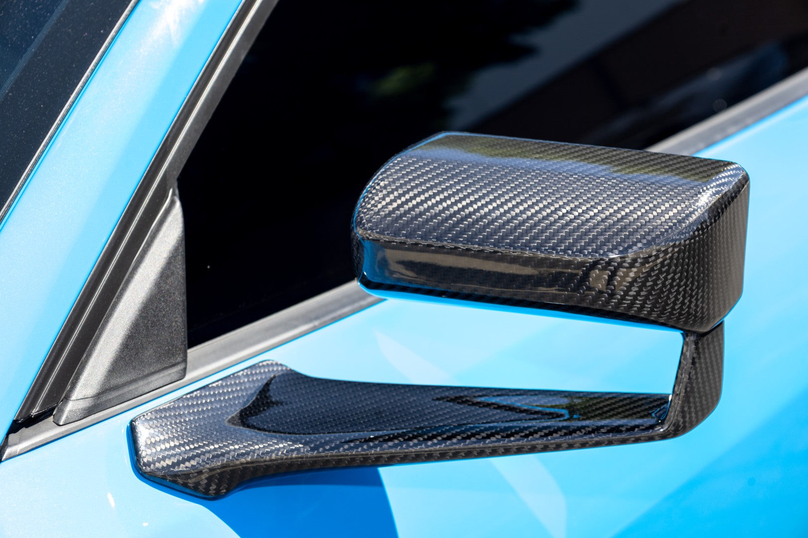 Carbon fiber side mirror with twill weave pattern mounted on blue vehicle door panel - APR Performance side mirror for Ford S650 Mustang Dark Horse