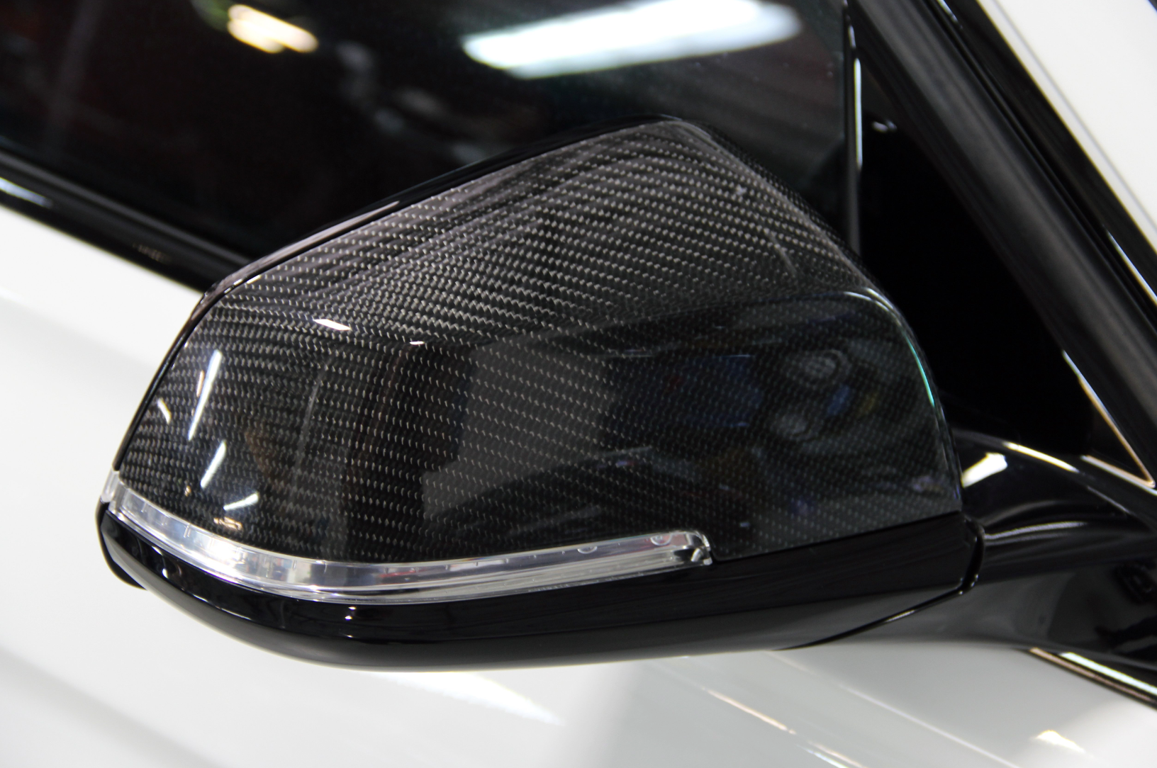 A close up view of one of the mirror of the Dinan Mirror Cap Set for BMW fitted on a white car
