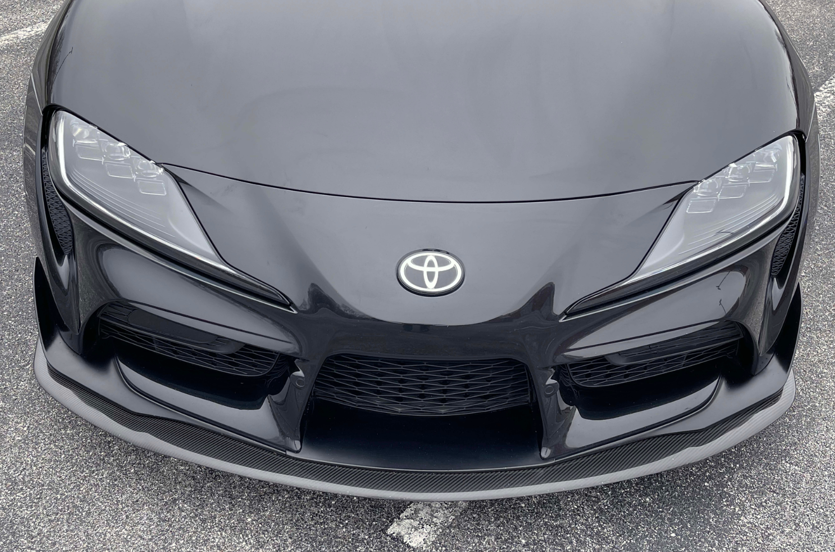 A close up top view of Dinan Front Lip for Toyota GR Supra 2020-2025 fitted on a black car on the road