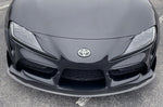 A close up top view of Dinan Front Lip for Toyota GR Supra 2020-2025 fitted on a black car on the road