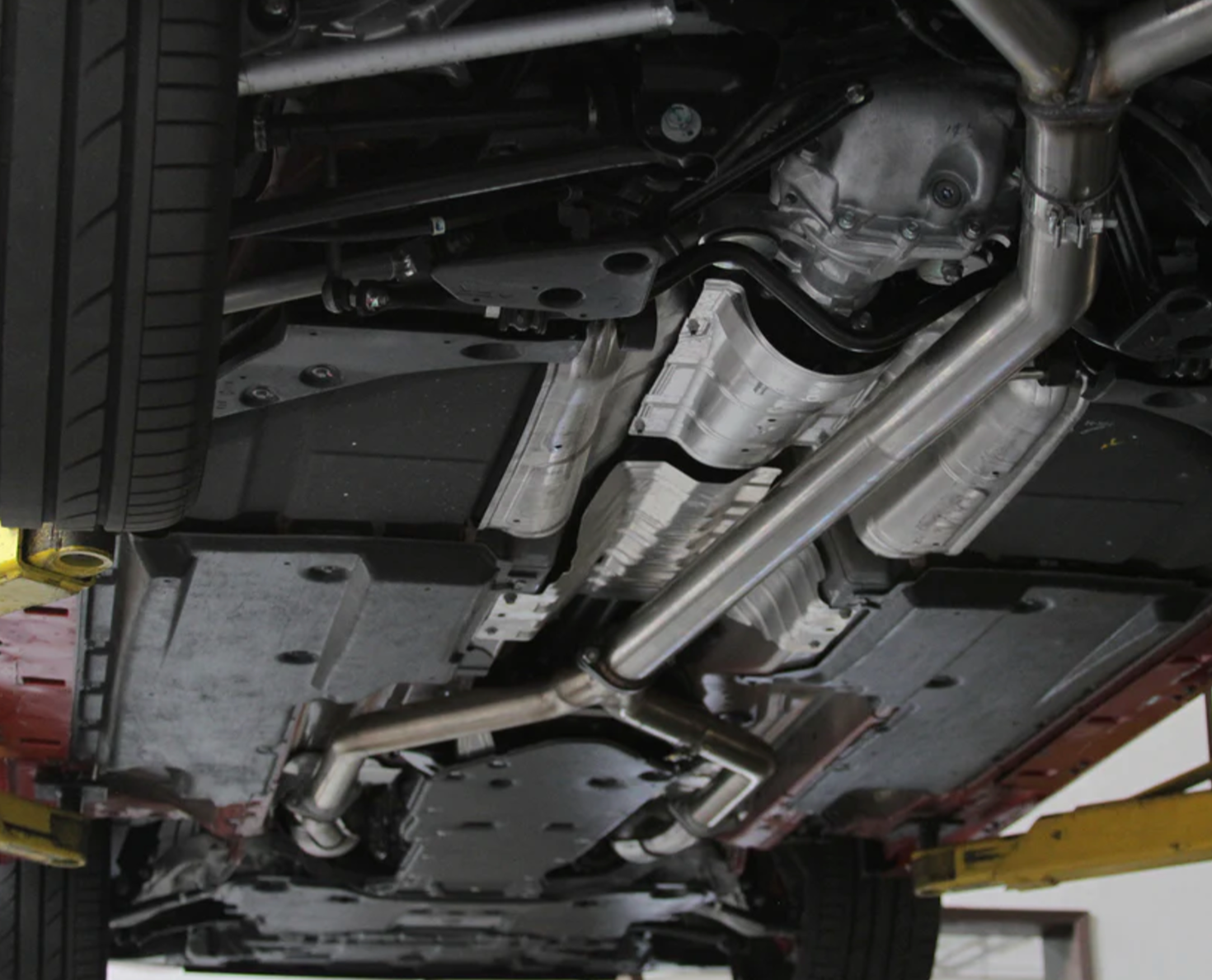 A view of the Stillen Cat-Back Exhaust System w/ (Polished / Burnt / Carbon Tips) for Infiniti Q60 3.0t 2017-2022 fitted on a lifted car from underneath