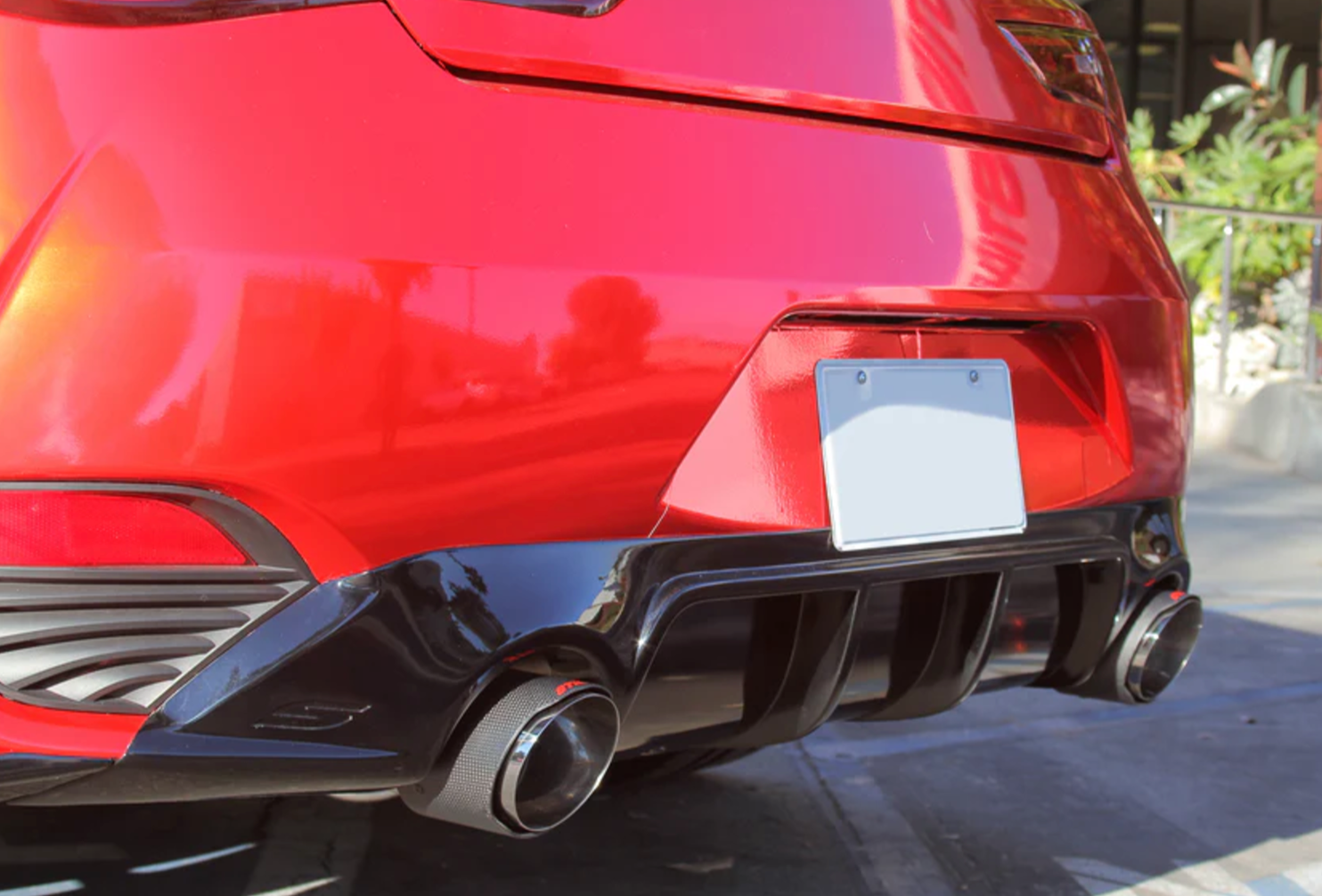 A view of the carbon tips fitted on the back of a red car of the Stillen Cat-Back Exhaust System w/ (Polished / Burnt / Carbon Tips) for Infiniti Q60 3.0t 2017-2022 