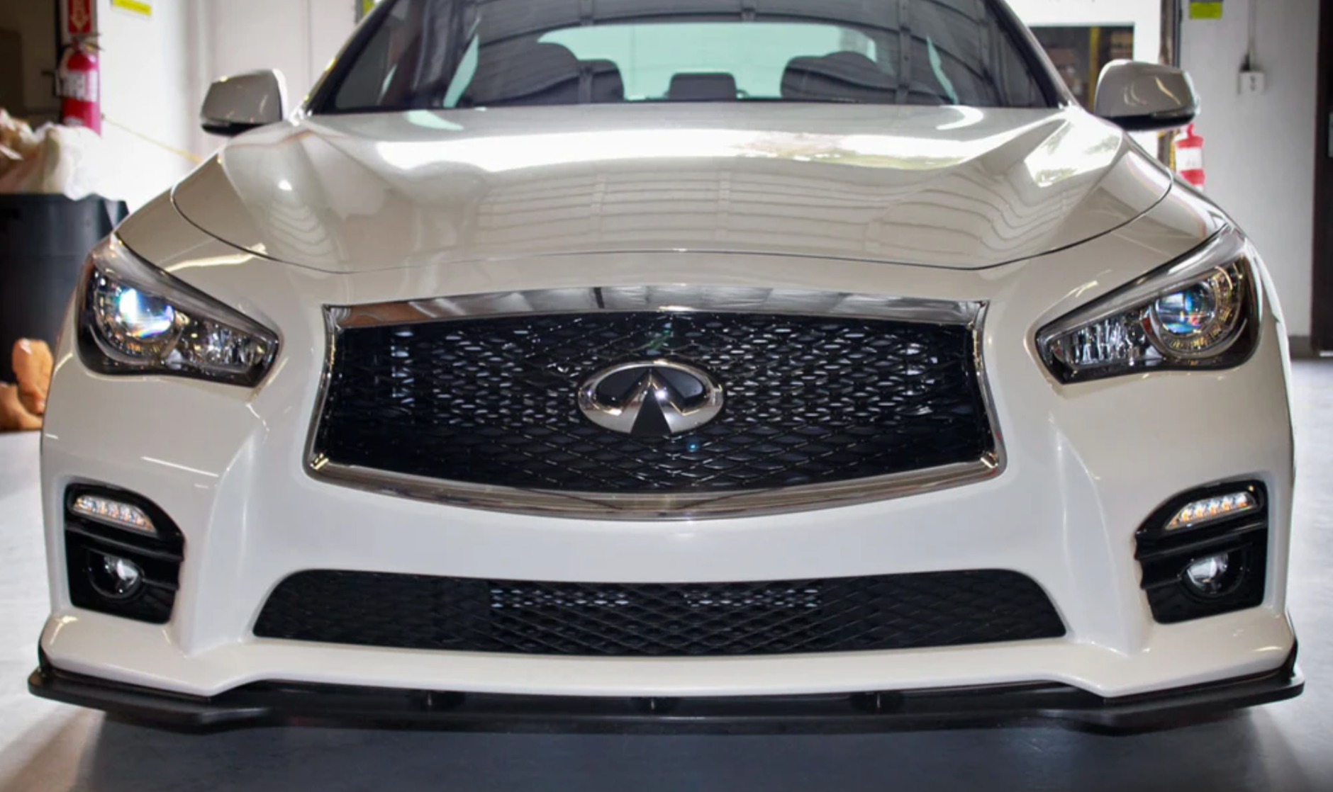 A front wide view of a white car fitted with Stillen Front Splitter for Infiniti Q50 Sport 2014-2017 on the ground